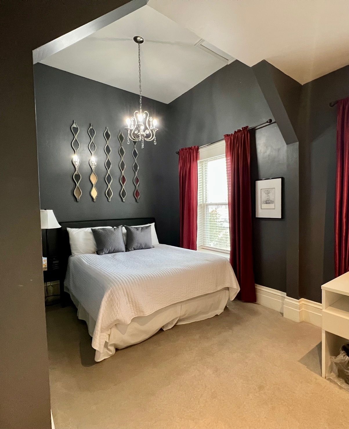 Dark bedroom with a bed, chandelier, and red curtains.
