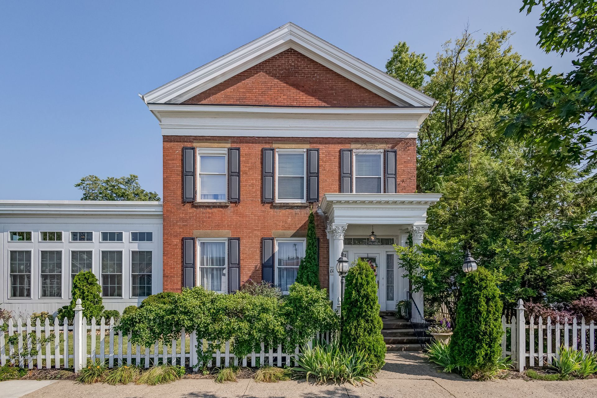 Two-story brick house with white trim, shutters, and a picket fence on a sunny day.