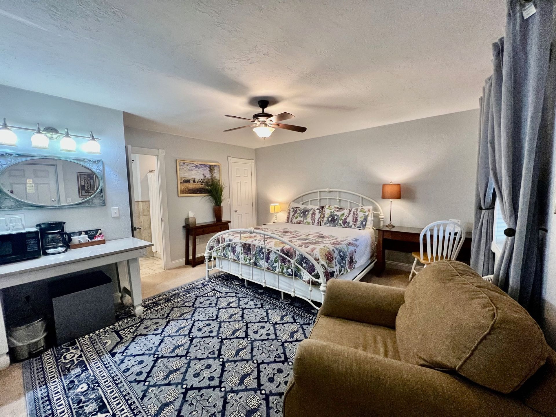 Bedroom with bed, rug, armchair, table, and a small kitchenette area.