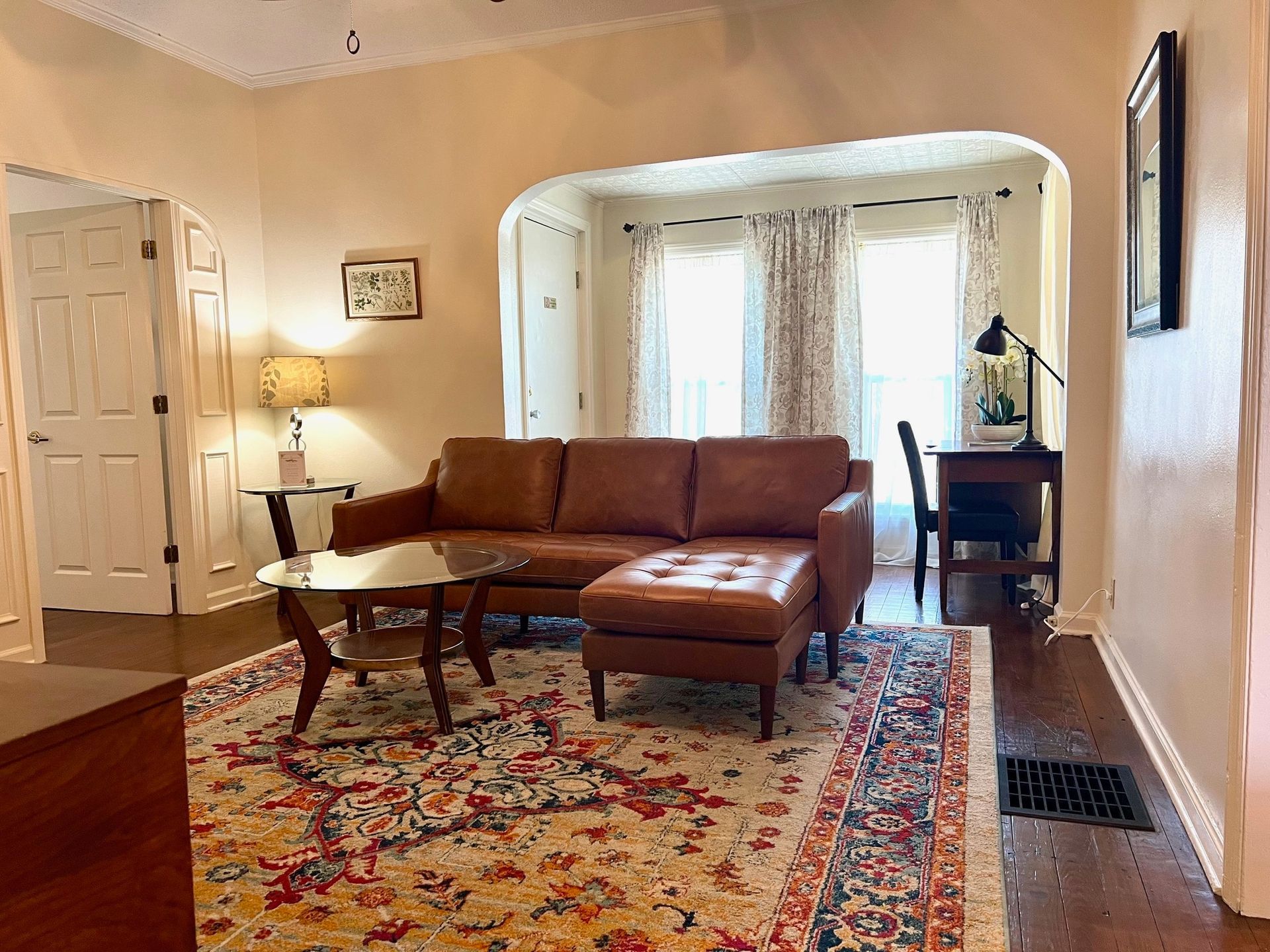 Living room with brown leather sectional, patterned rug, and desk by a window.