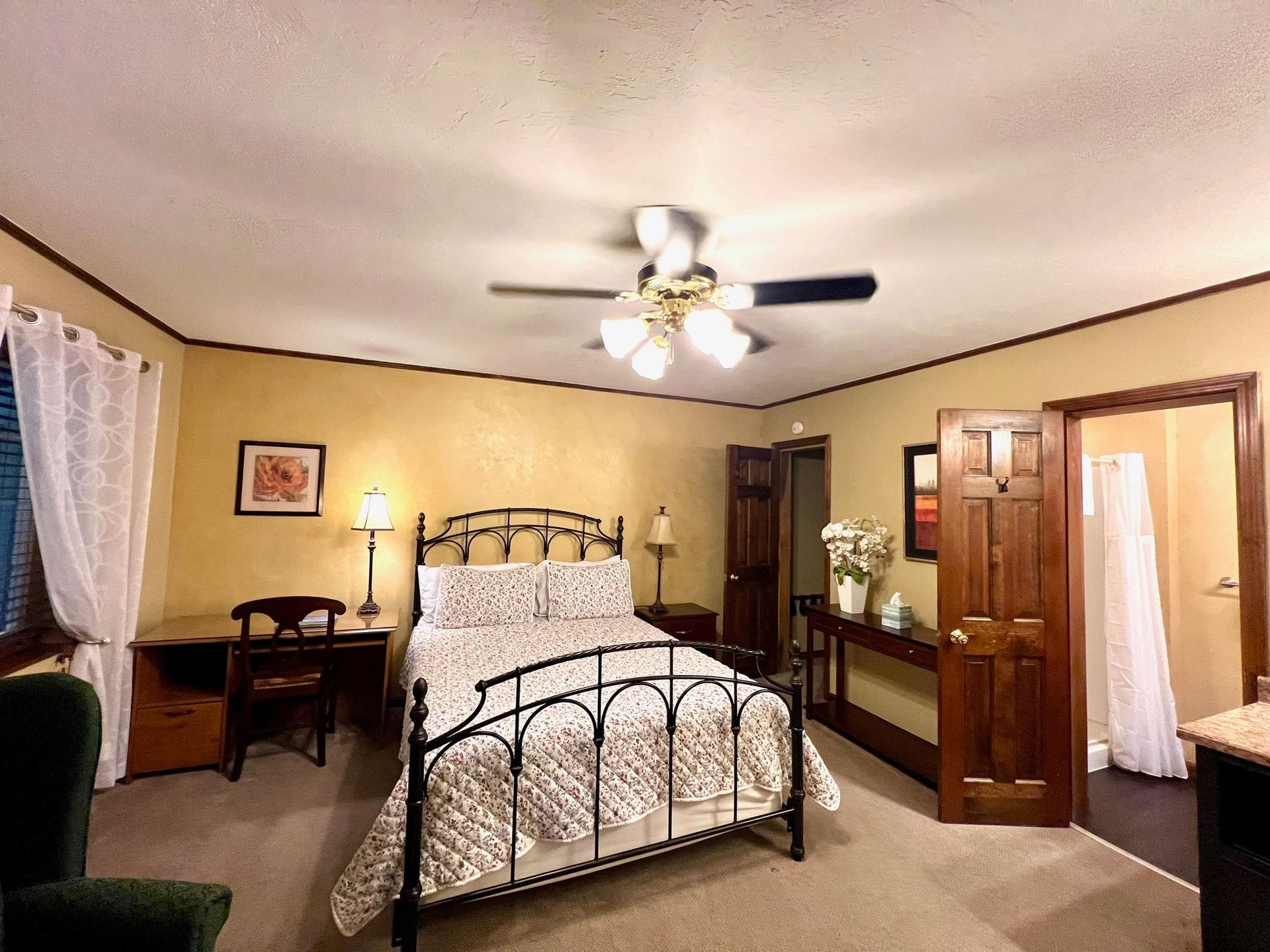 Bedroom with a wrought-iron bed, desk, and open doorways to a bathroom and another room.