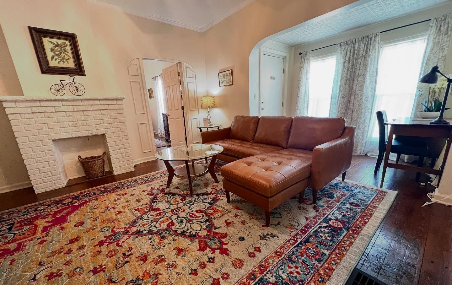 Living room with brown leather sectional, patterned rug, fireplace, and desk by a window.