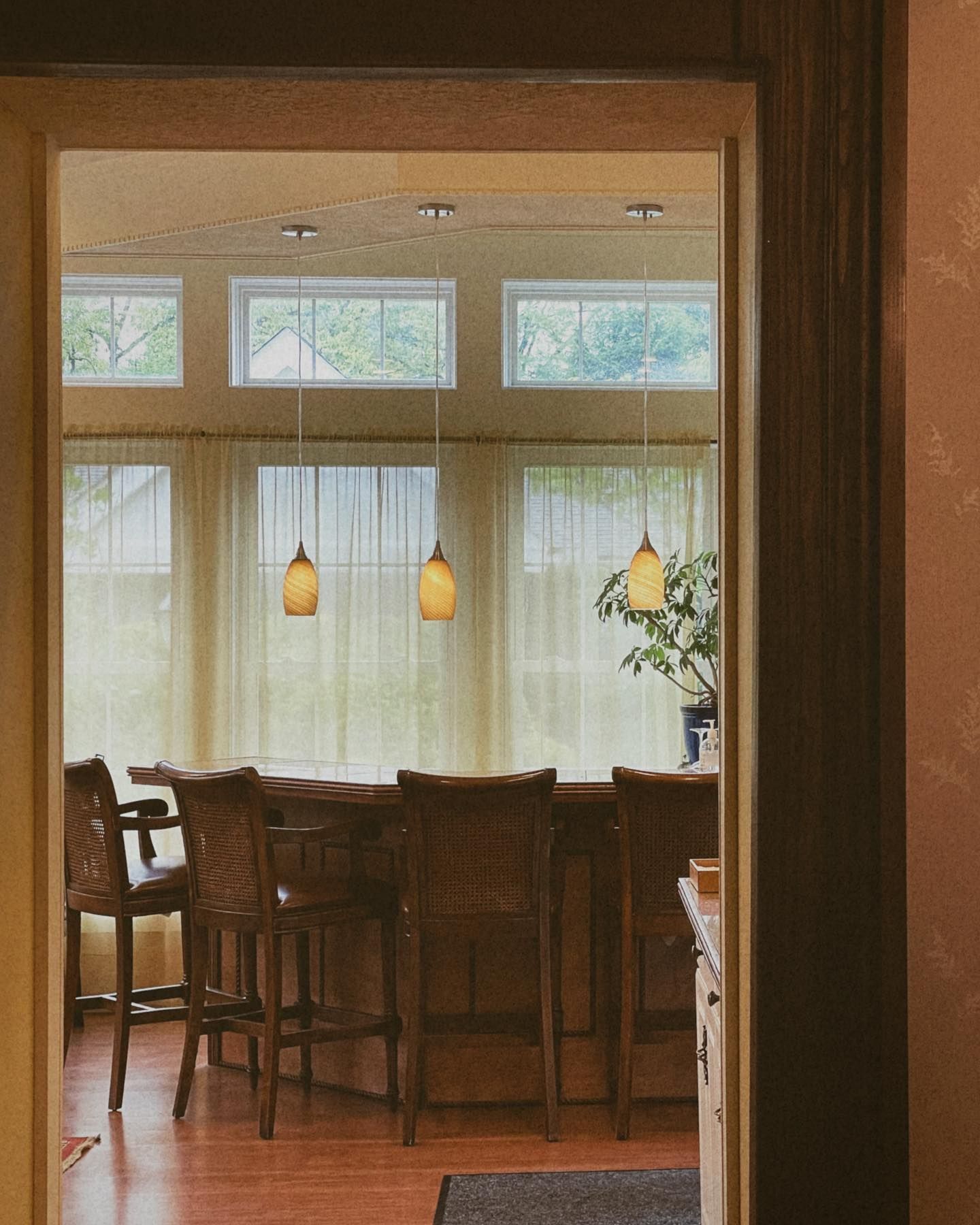 Wooden bar with stools inside a room with windows and pendant lights, seen from a doorway.
