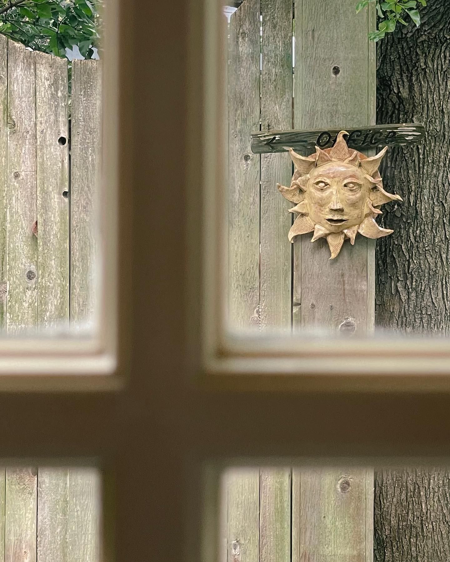 Window view of wooden fence with sun-shaped wall decoration.