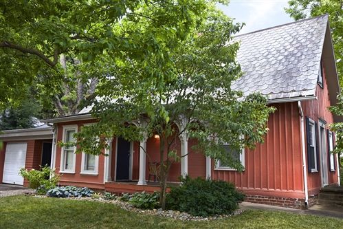 Red house with white trim, porch, and a tree in front.