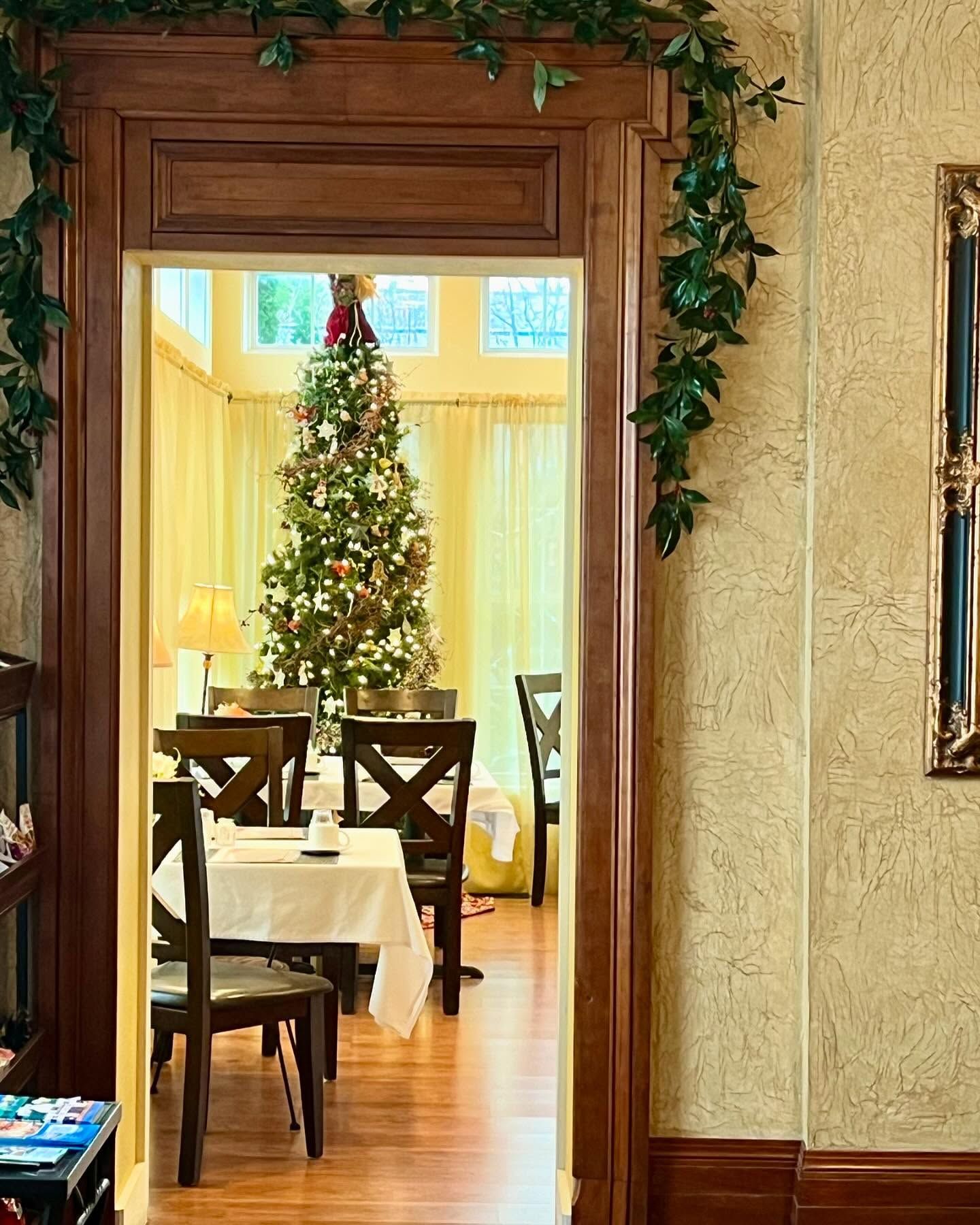 An open doorway into a dining room with a decorated Christmas tree. A table is set. Brown trim and green garland.