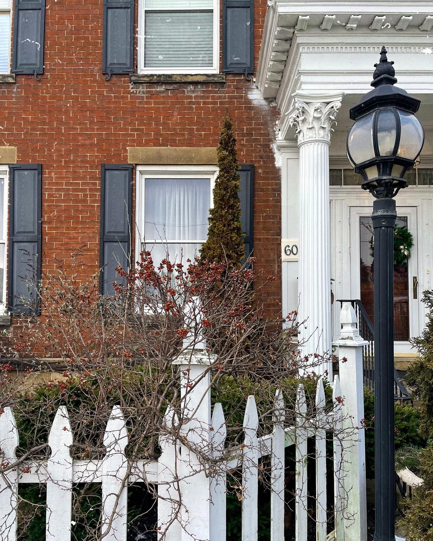 Red brick building with white pillars and picket fence; black shutters and street lamp.