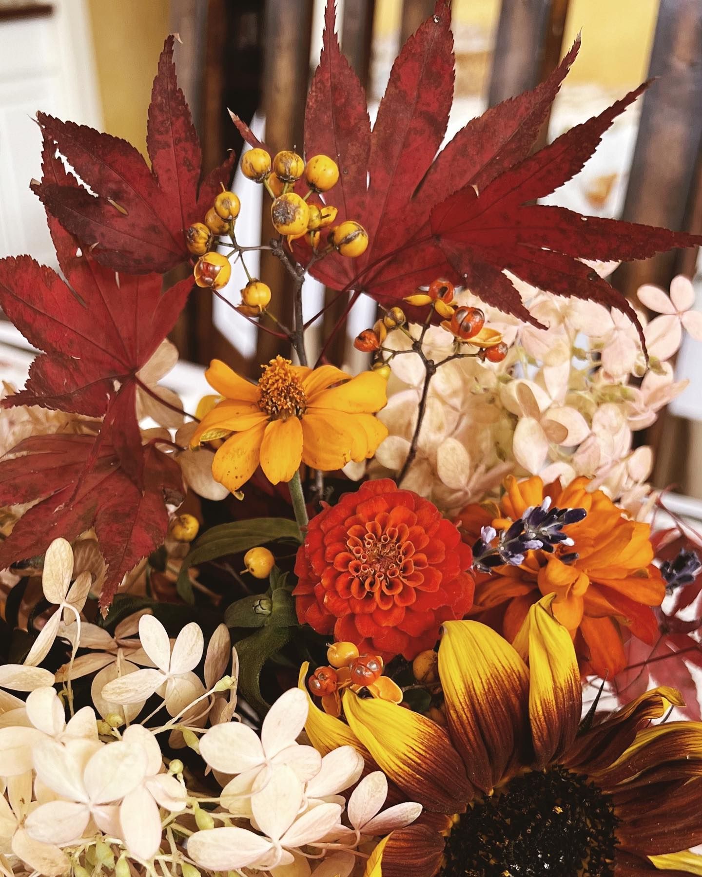 Autumn floral arrangement of red maple leaves, sunflowers, orange and yellow flowers.