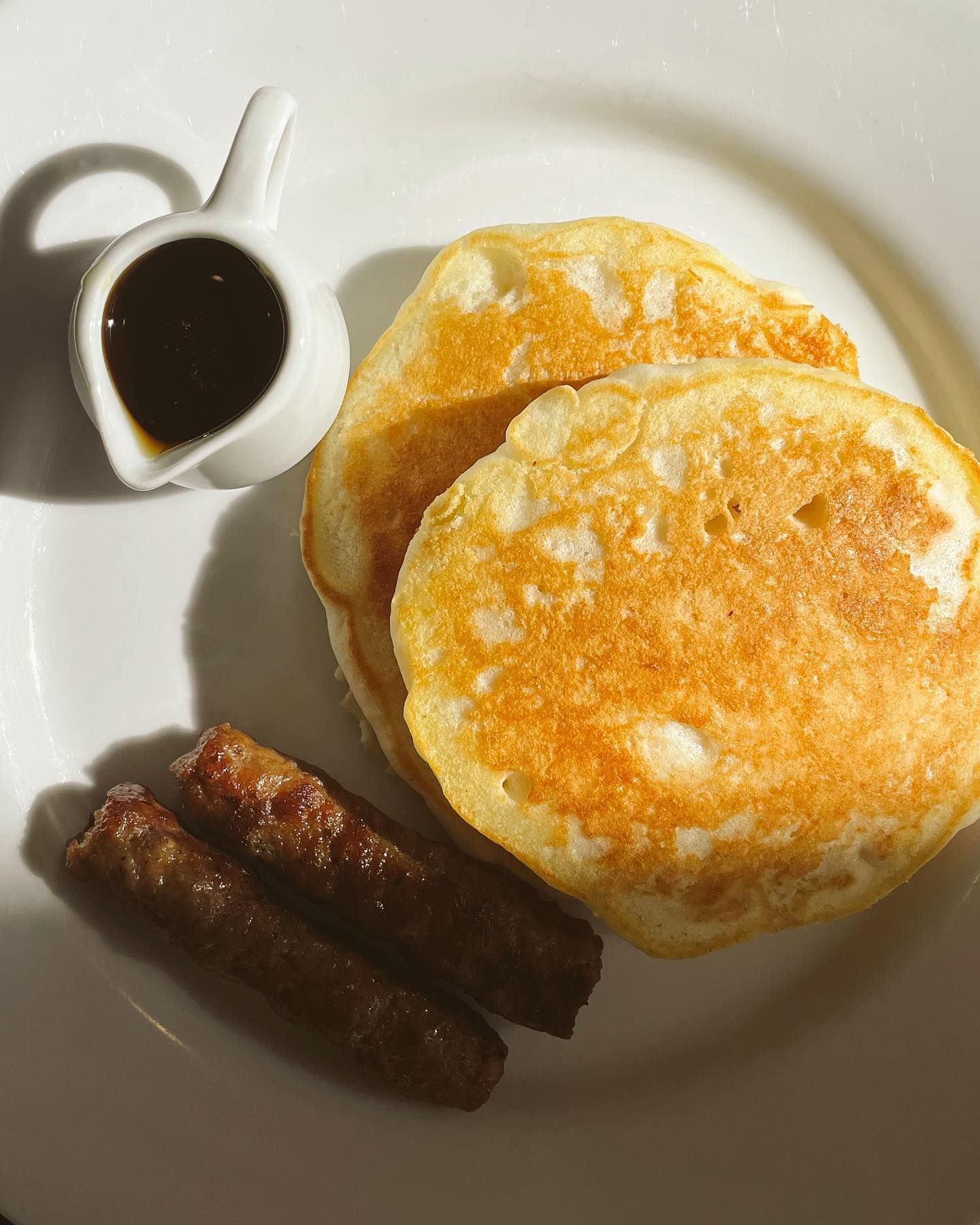 Pancakes with sausage and syrup on a white plate.