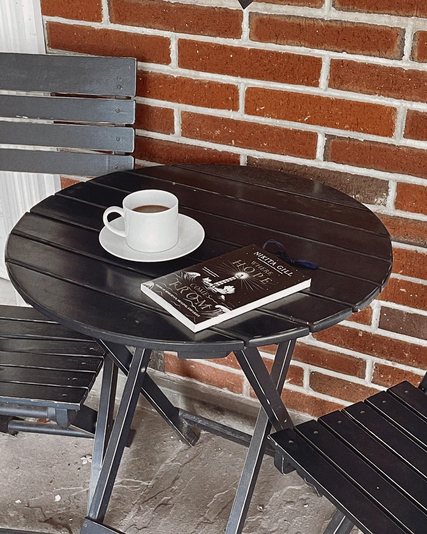A dark table with a coffee cup and a book, next to a brick wall.