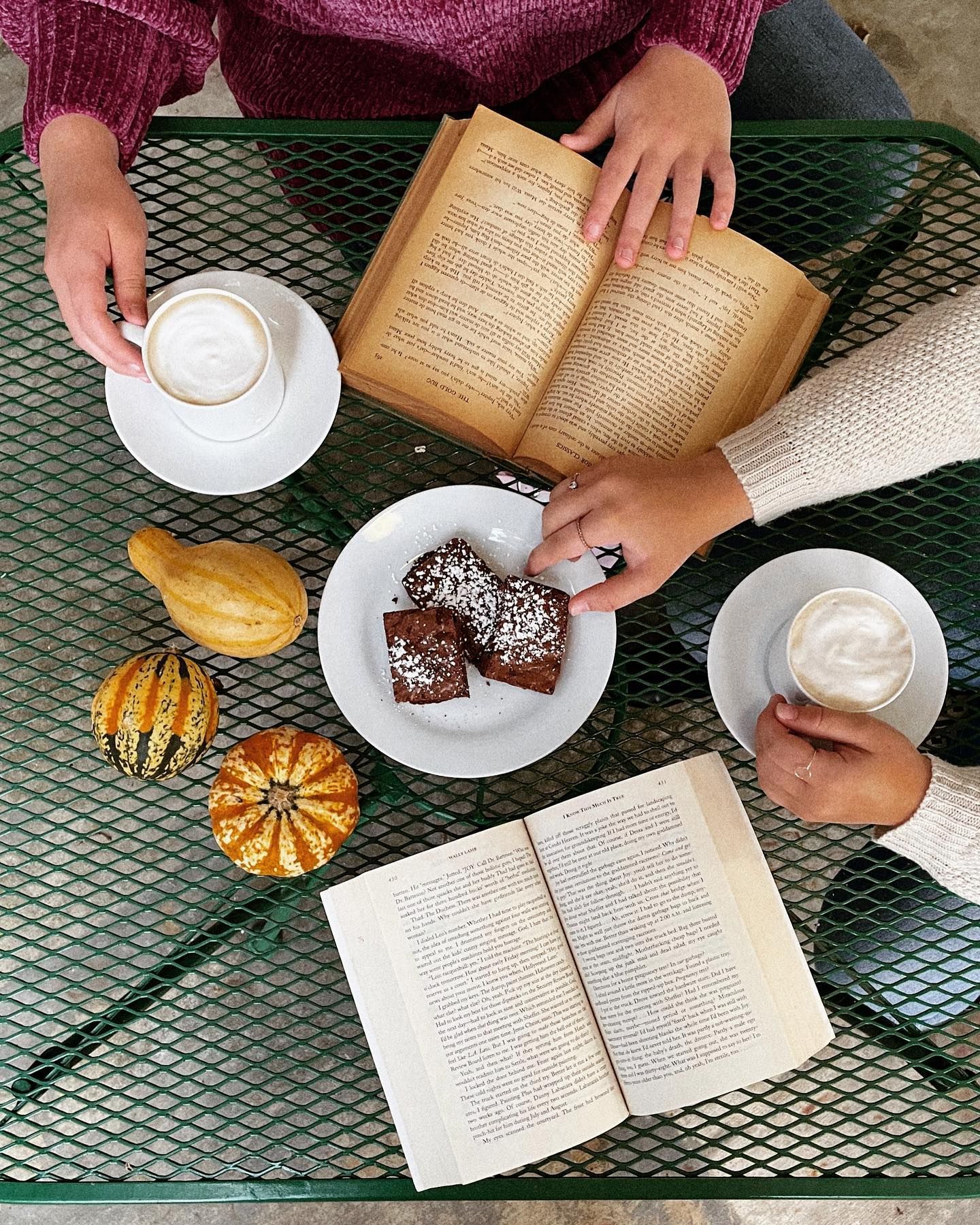 People at table with coffee, books, and treats; autumn gourds.