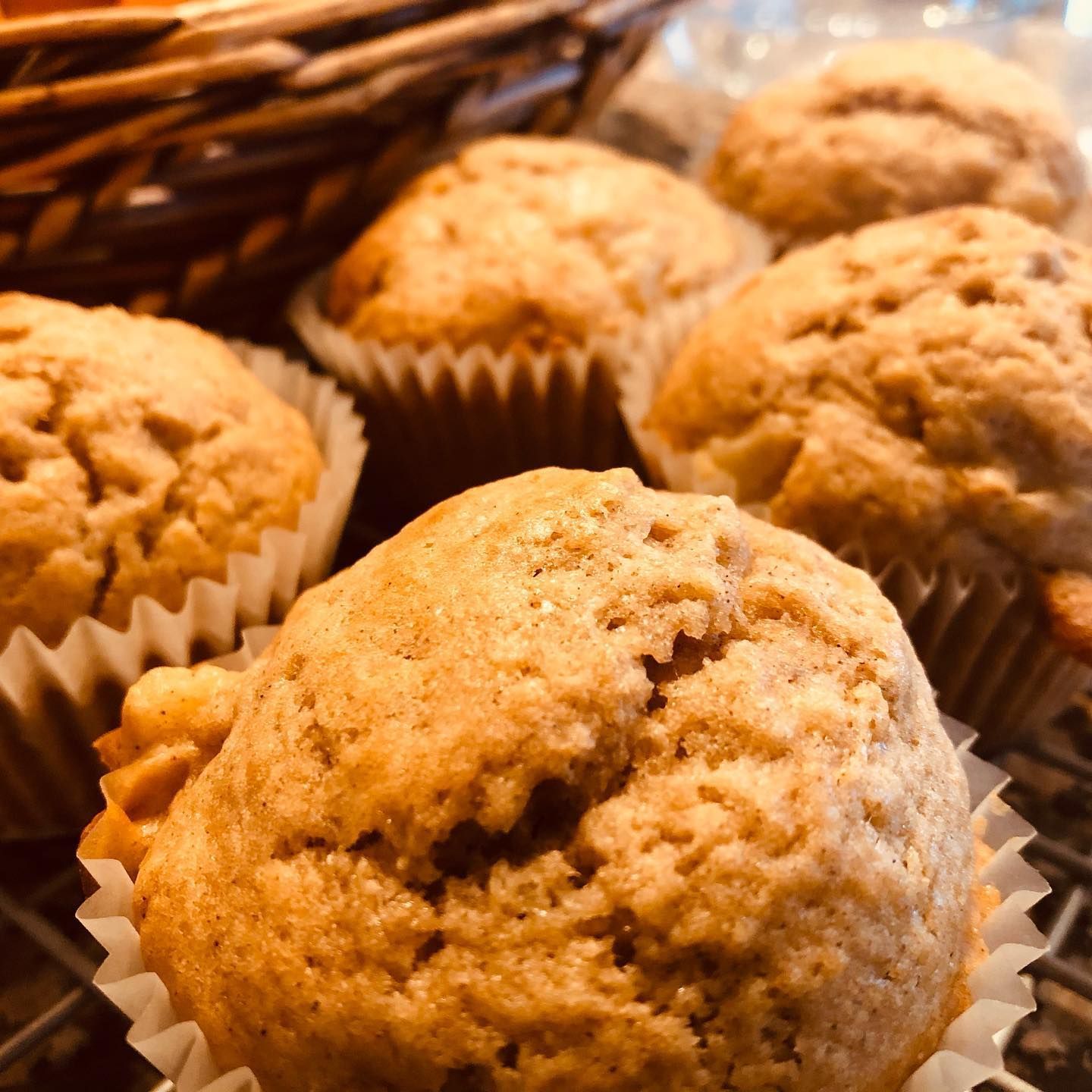 Six golden-brown muffins in white paper liners, on a wire rack, with a wicker basket in the background.