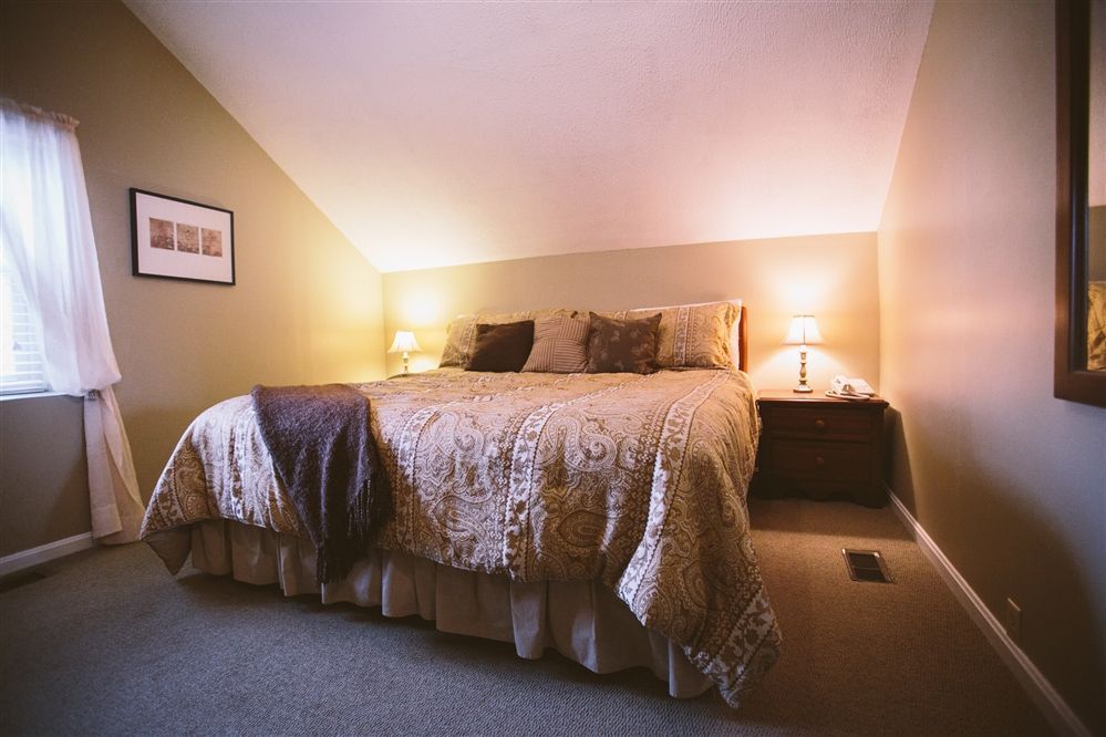 Bedroom with a bed, nightstand, window, and angled ceiling. Soft lighting and neutral colors.