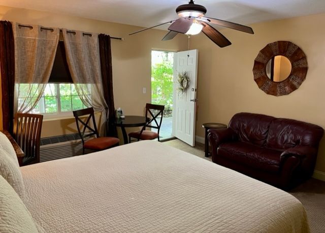 A beige-walled hotel room with a bed, small table and chairs, a couch, and a doorway to an outdoor patio.