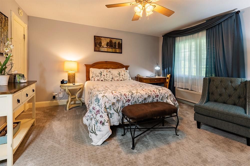 Bedroom with bed, desk, chair, and dresser, decorated in neutral colors with floral bedding.