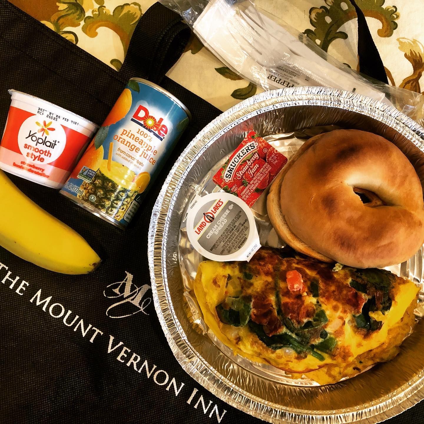 Breakfast with a bagel, omelet, fruit, juice, yogurt, and cutlery in a Mount Vernon Inn bag.