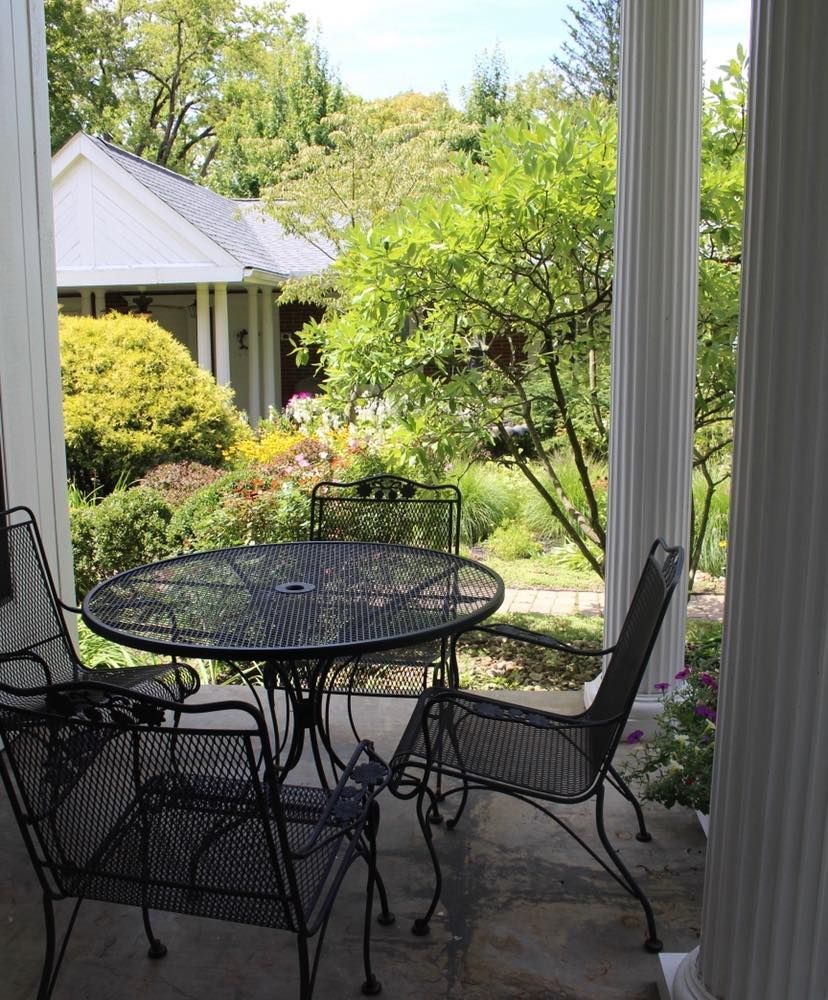 Wrought iron patio table and chairs on a porch with garden view, sunny day.