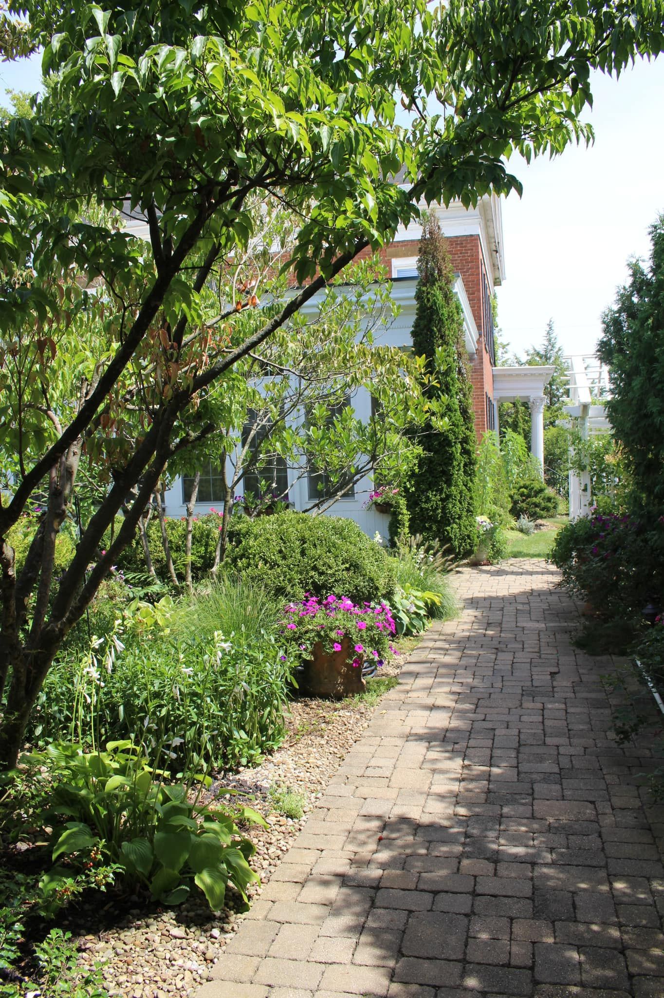 Brick pathway through a lush garden leads to a light blue house with white trim.