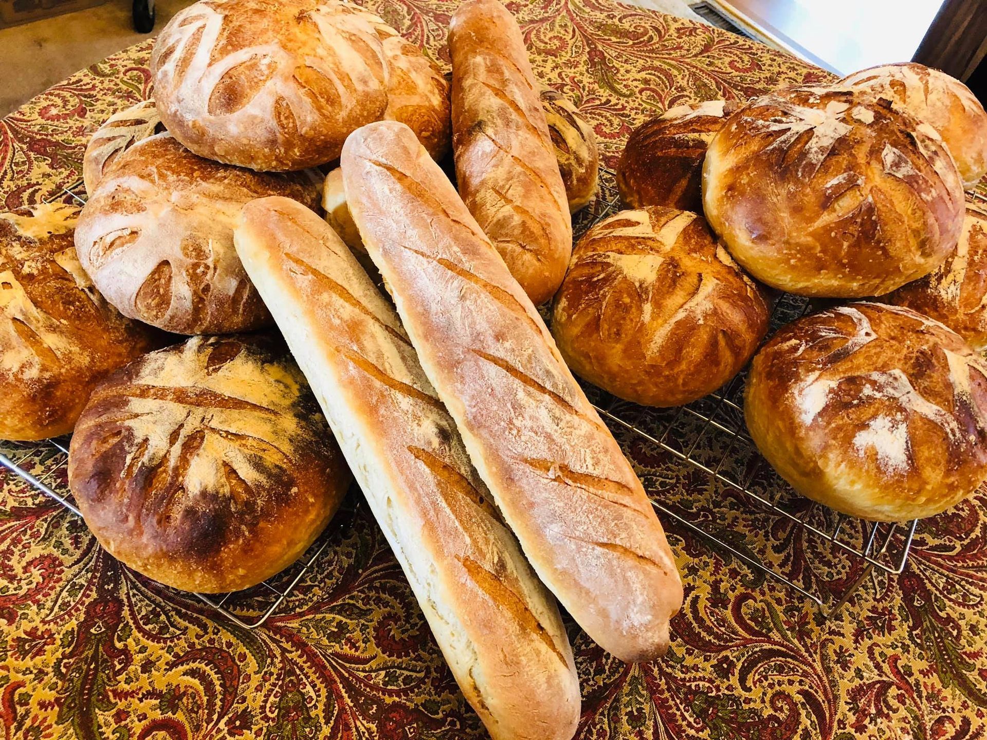 Assortment of fresh baked bread, including baguettes and round loaves, on a patterned surface.