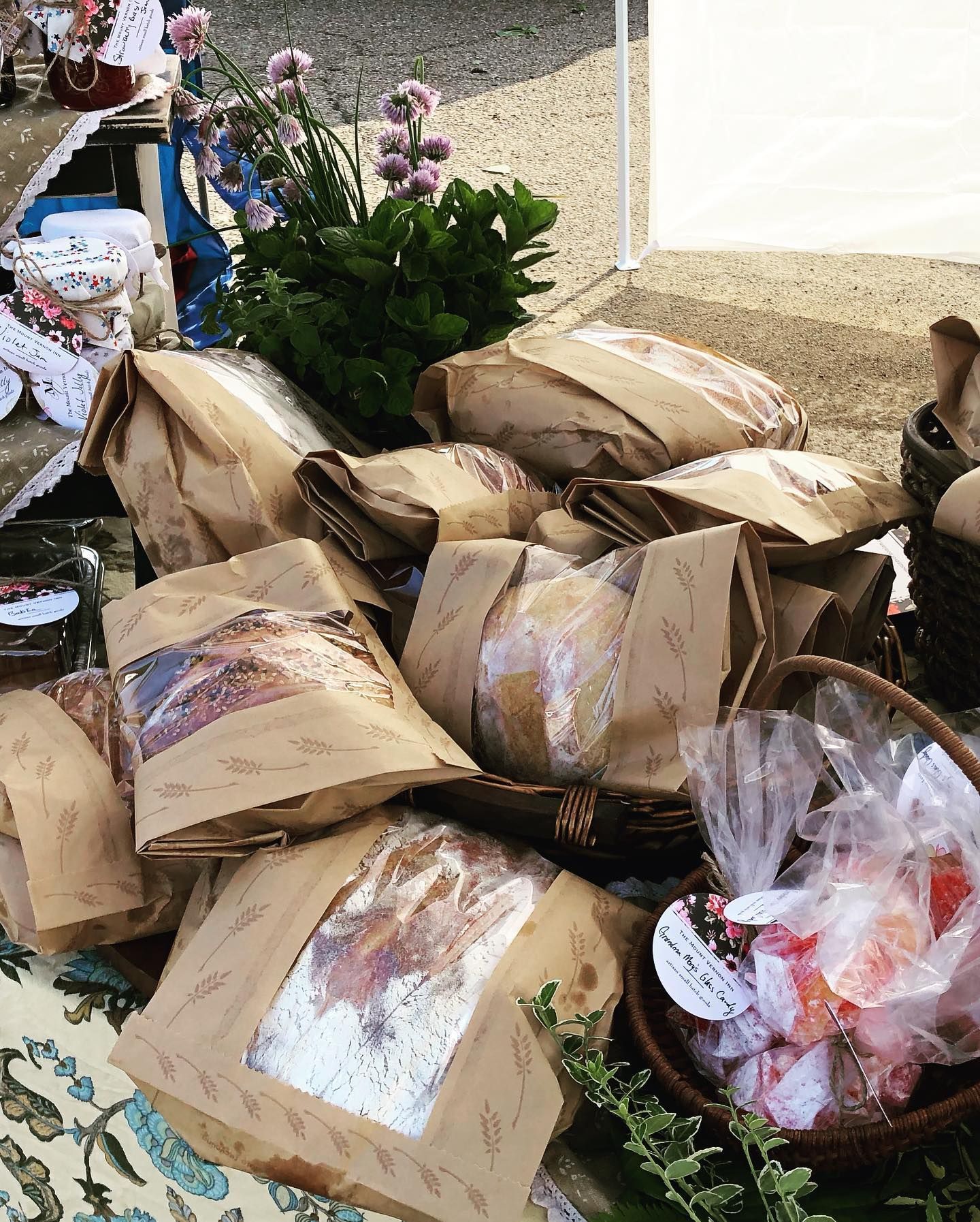 Bags of food, wrapped in brown paper, on a table at a farmer's market, with flowers and baskets.