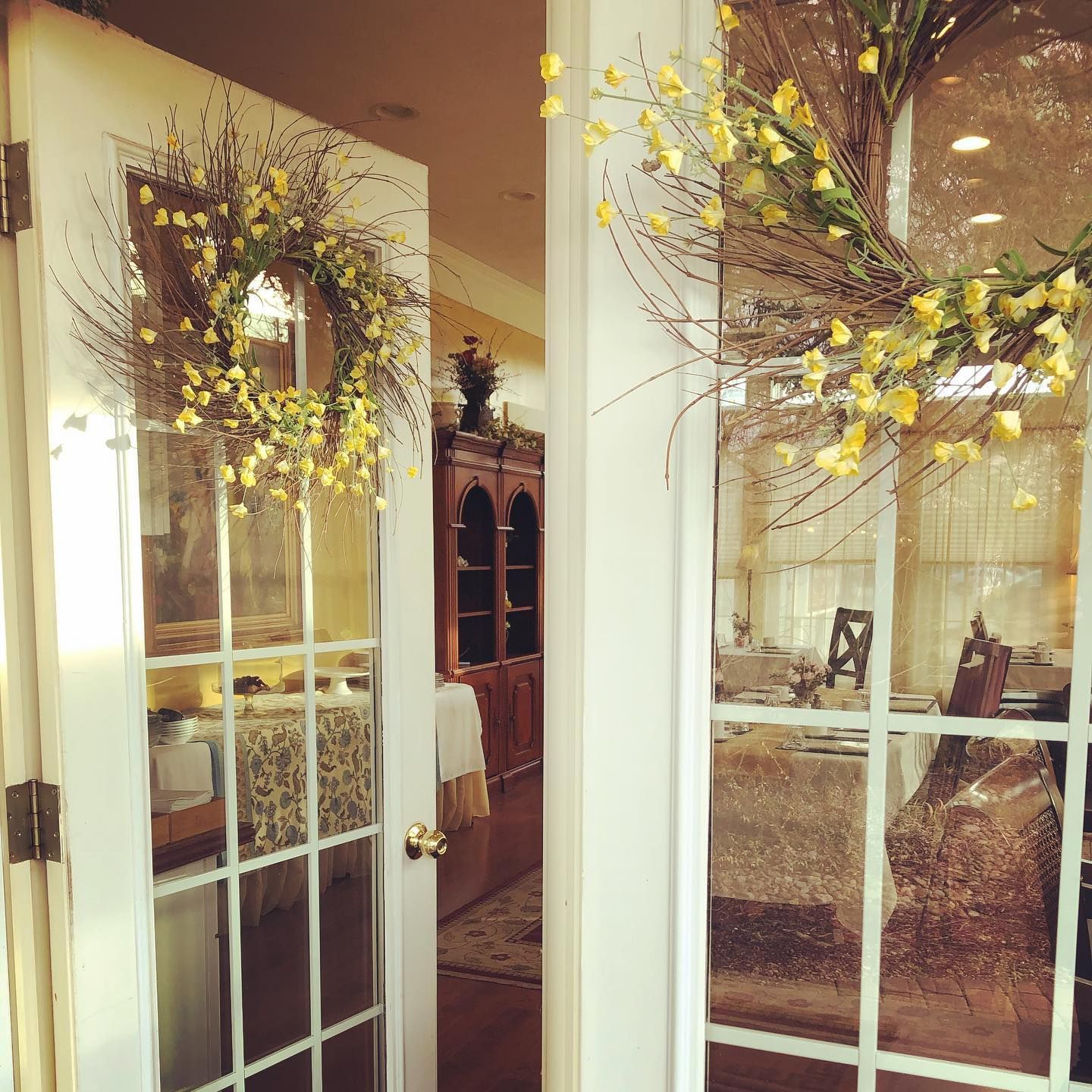 French doors with yellow floral wreaths, opening to a sunlit dining area.
