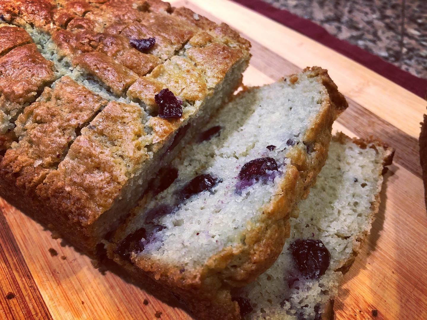 Sliced cranberry bread on a wooden cutting board, with visible fruit pieces within.