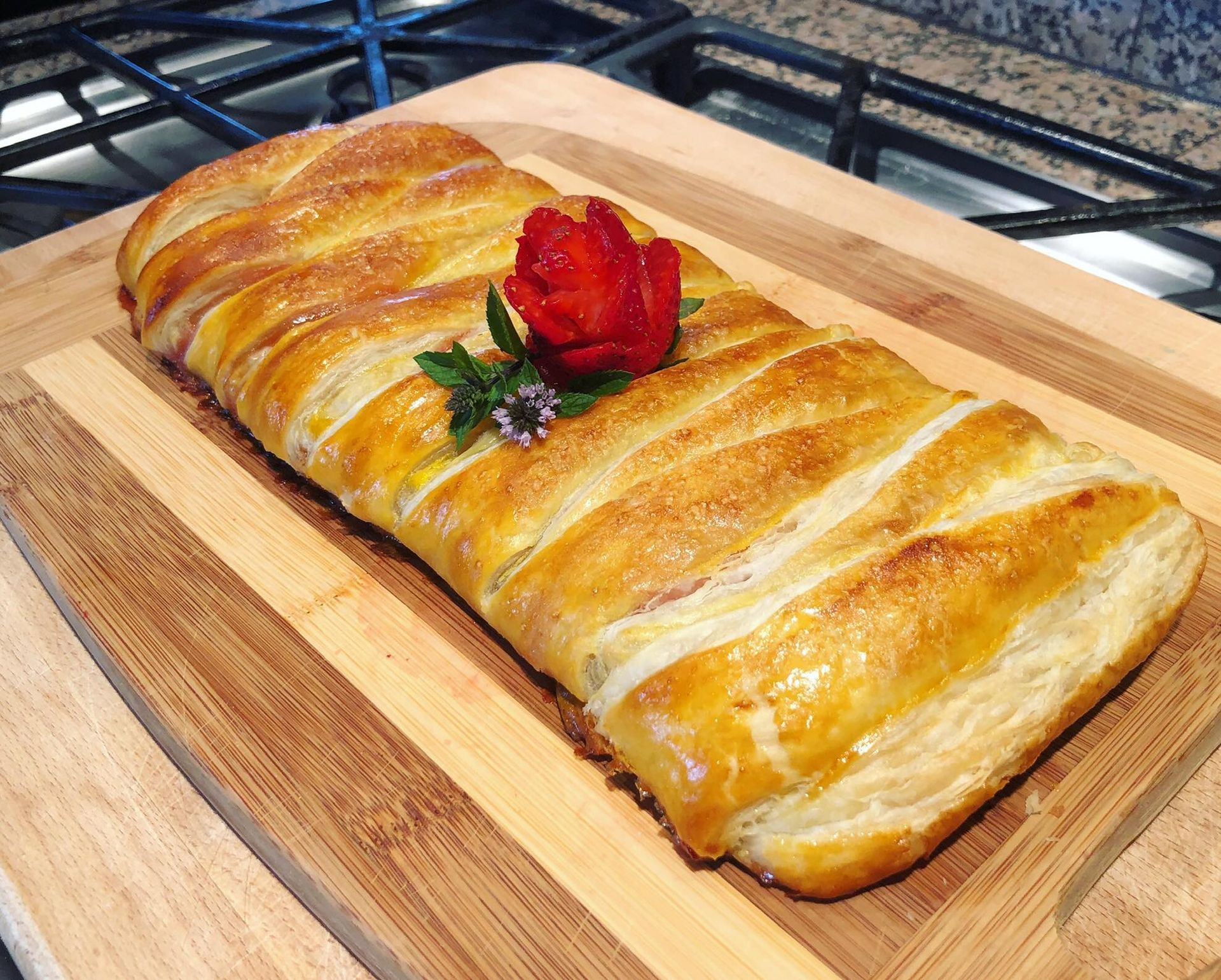 Pastry braid on wooden board, topped with strawberry rose and sprig of herbs.
