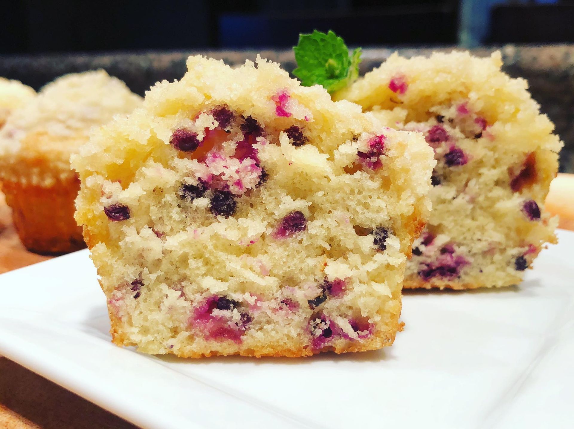 Blueberry muffin, cut open, revealing berries inside; white plate, other muffins in the background.