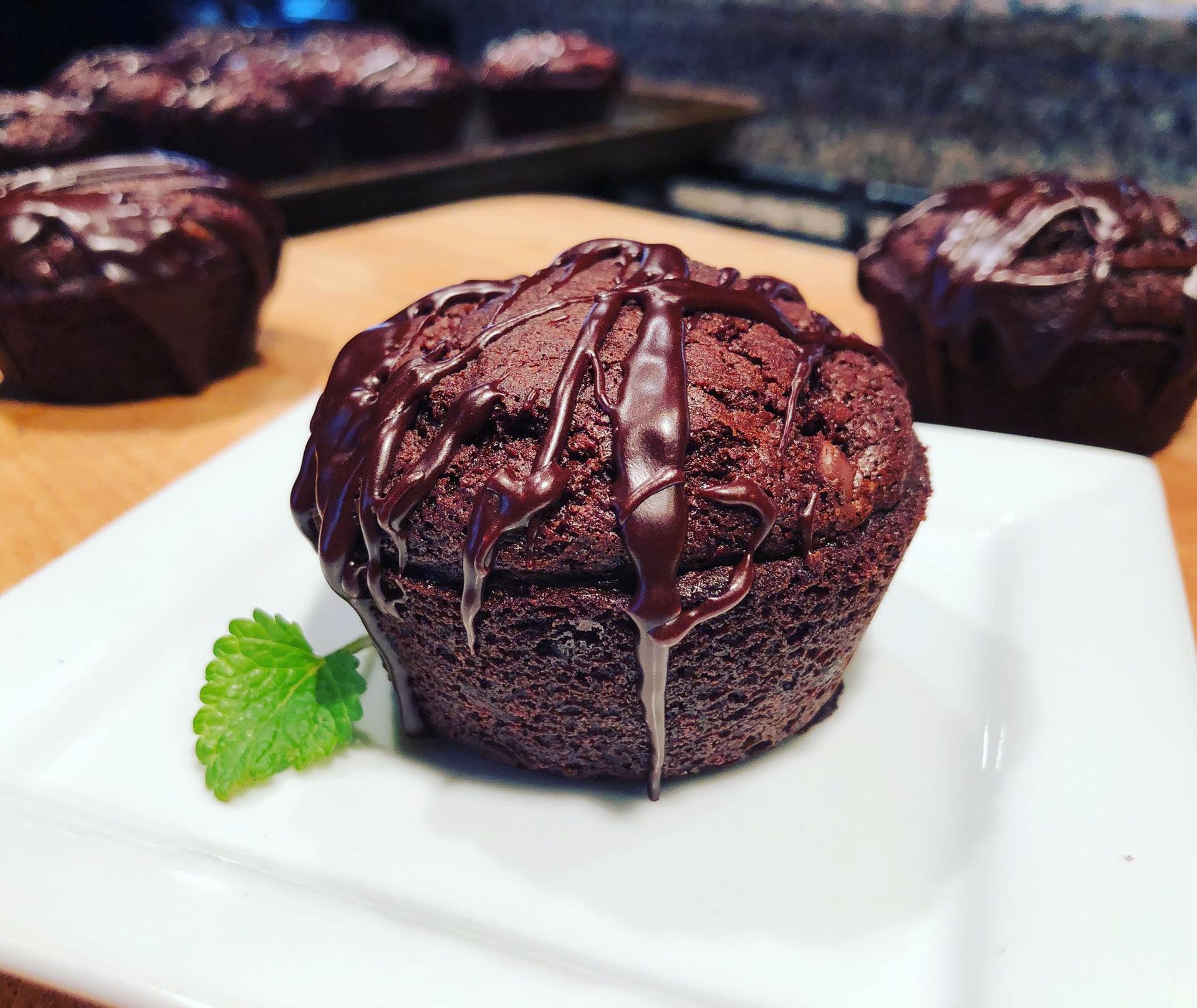 Chocolate muffin with chocolate drizzle on a white plate, mint sprig.