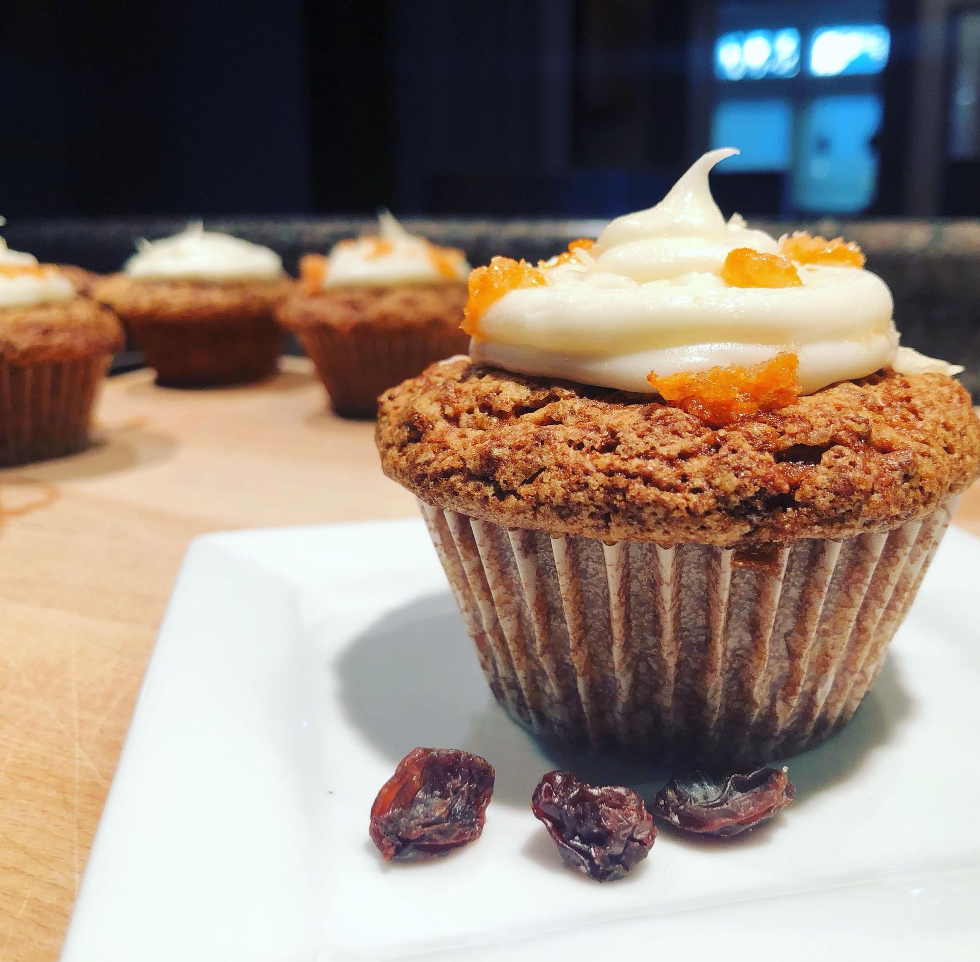 Carrot muffins topped with cream cheese frosting and orange zest, with cranberries on a white plate.