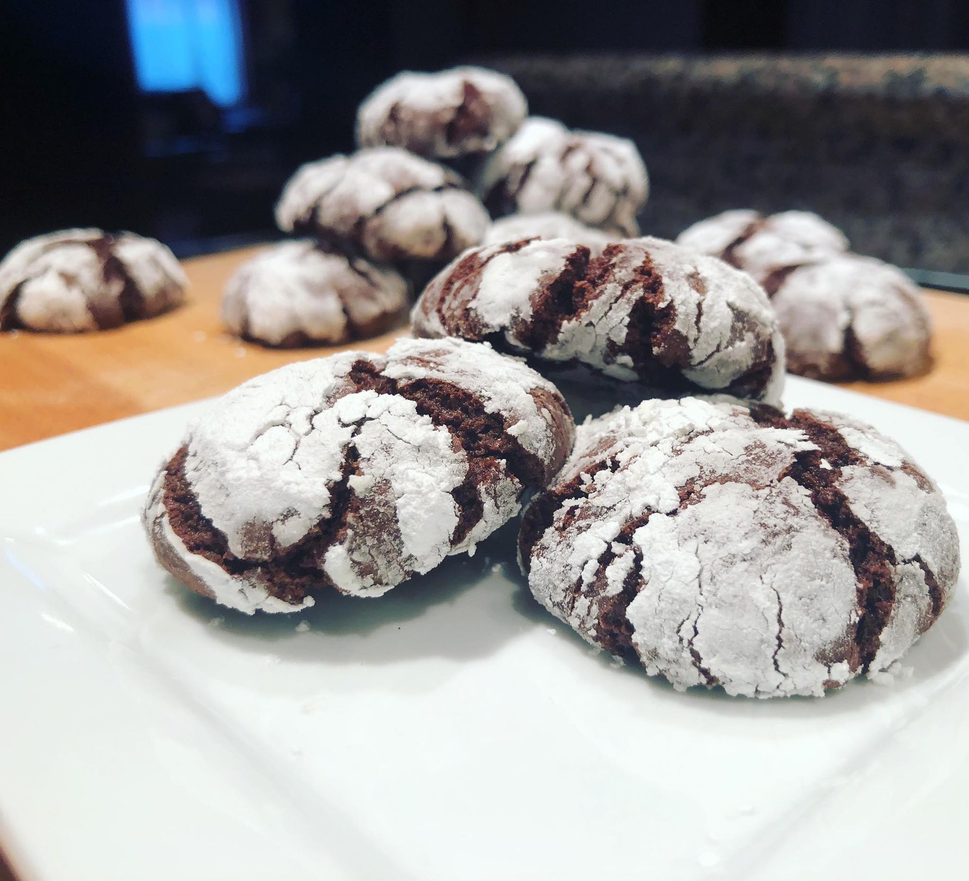 Chocolate crinkle cookies dusted with powdered sugar on a white plate with more cookies in the background.