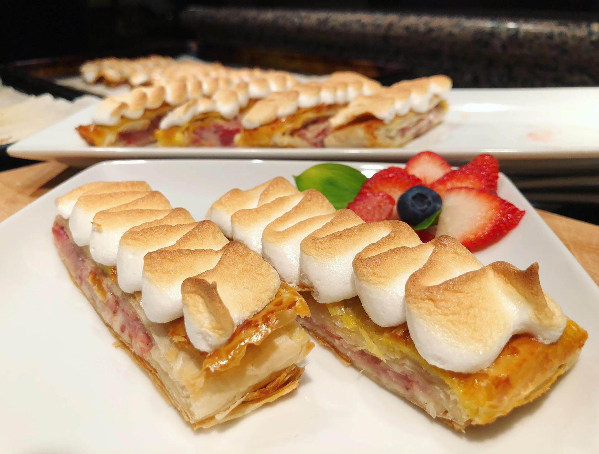 Two rectangular pastries topped with toasted meringue; served with fruit.