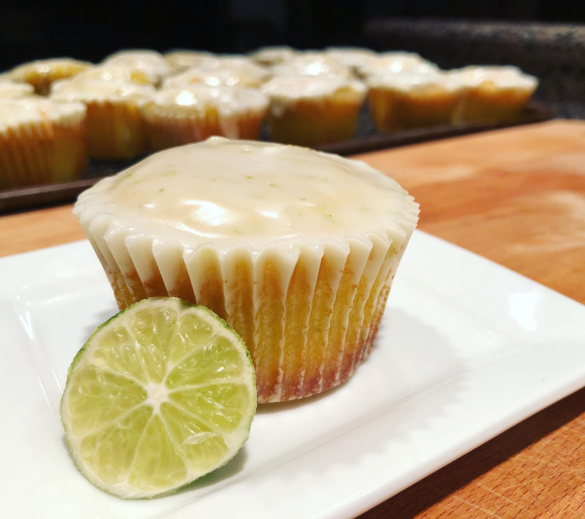 Lime cupcake with white glaze, half a lime, on a white plate. Cupcakes in background.