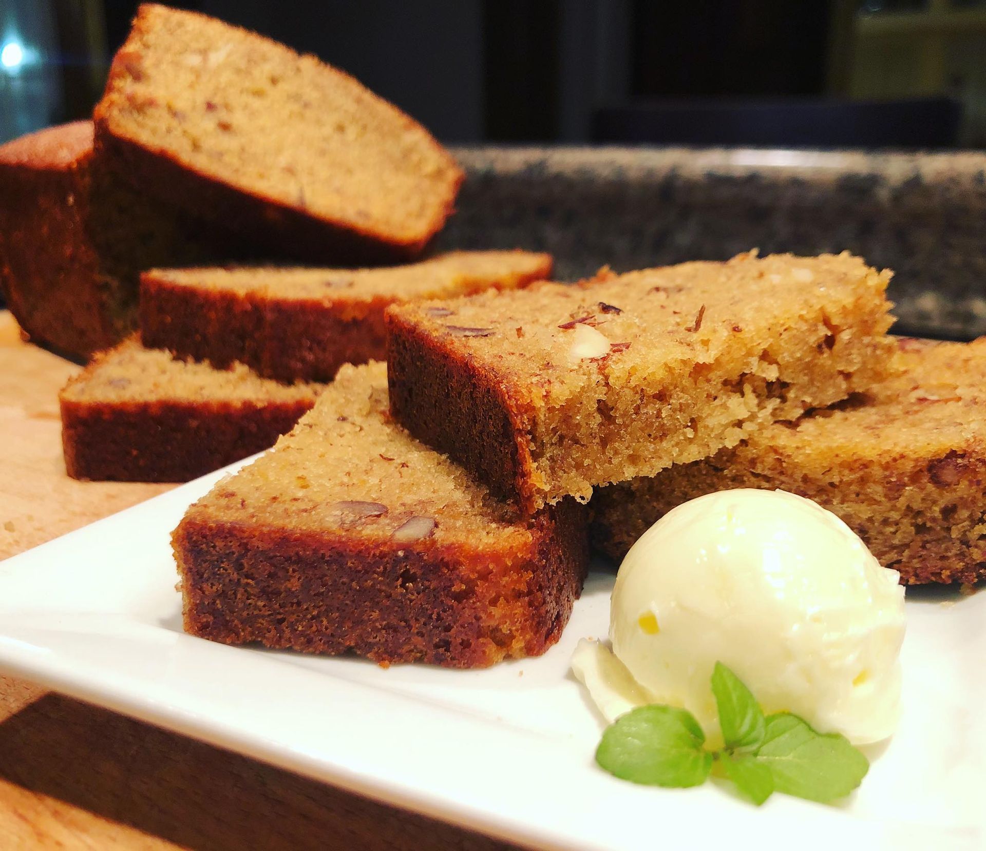 Slices of banana bread on a white plate with a scoop of yellow cream and green leaves.