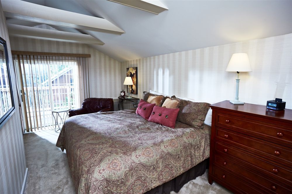Bedroom with striped wallpaper, bed, dresser, balcony door, and two lamps.