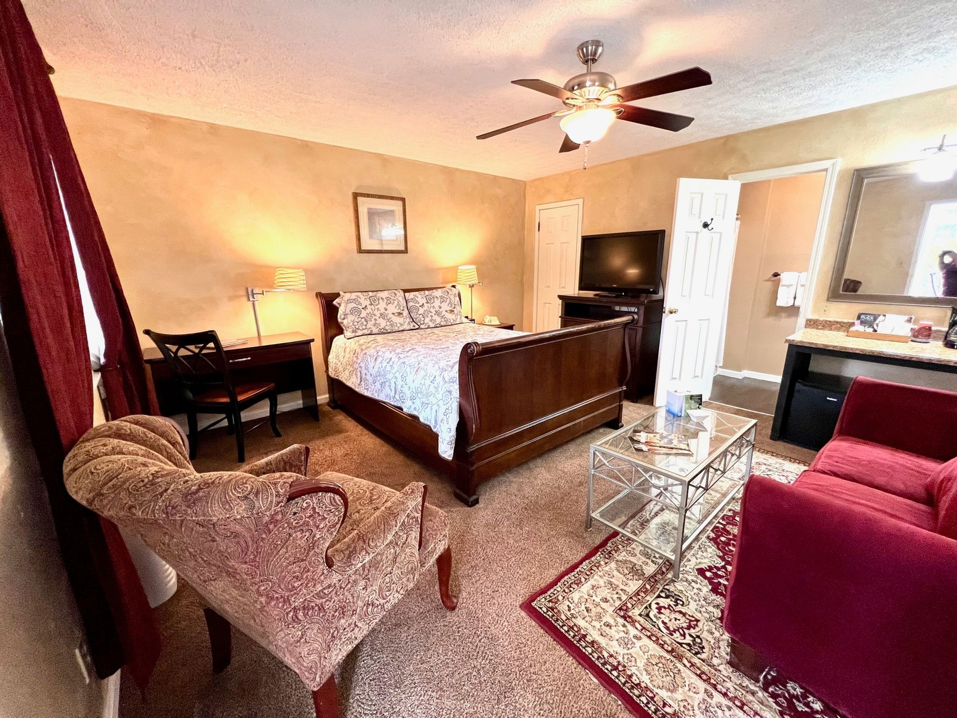 Bedroom with a dark wooden bed, red sofa, patterned chair, and a rug.