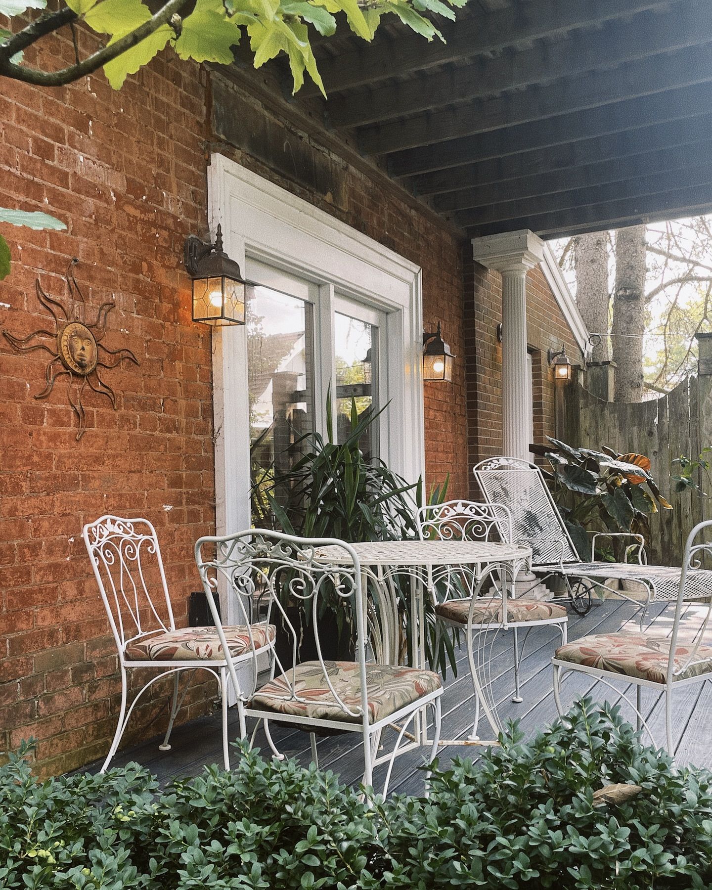 White patio furniture on a brick porch, with a sun decoration and sconce lights.