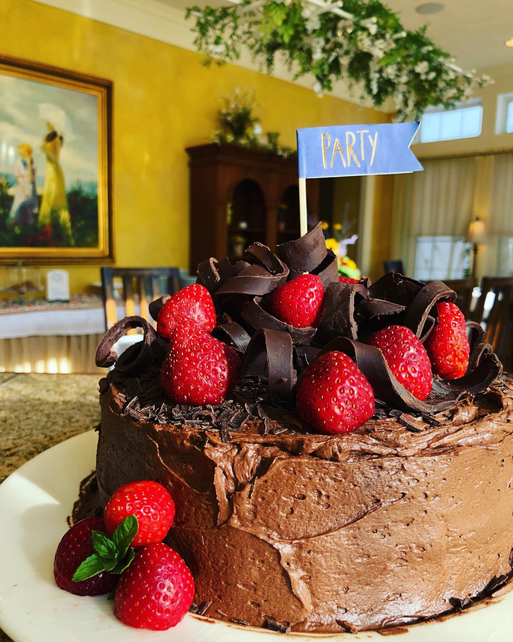 Chocolate cake topped with strawberries and chocolate shavings, decorated with a party flag.