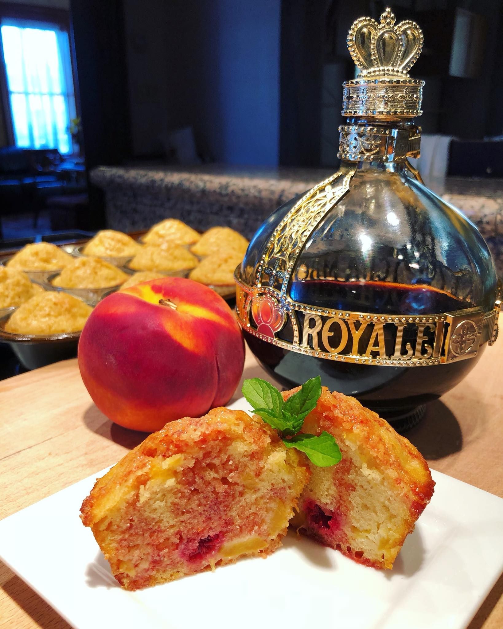 Peach muffins with a peach and Crown Royal bottle, on a counter, with more muffins in the background.