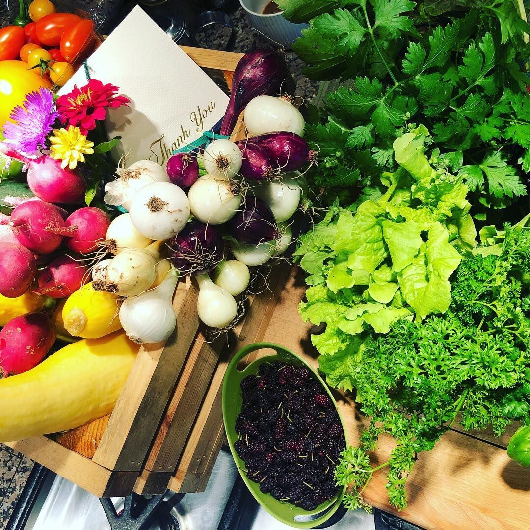 Fresh produce arrangement with radishes, onions, lettuce, herbs, and flowers on a wooden surface.