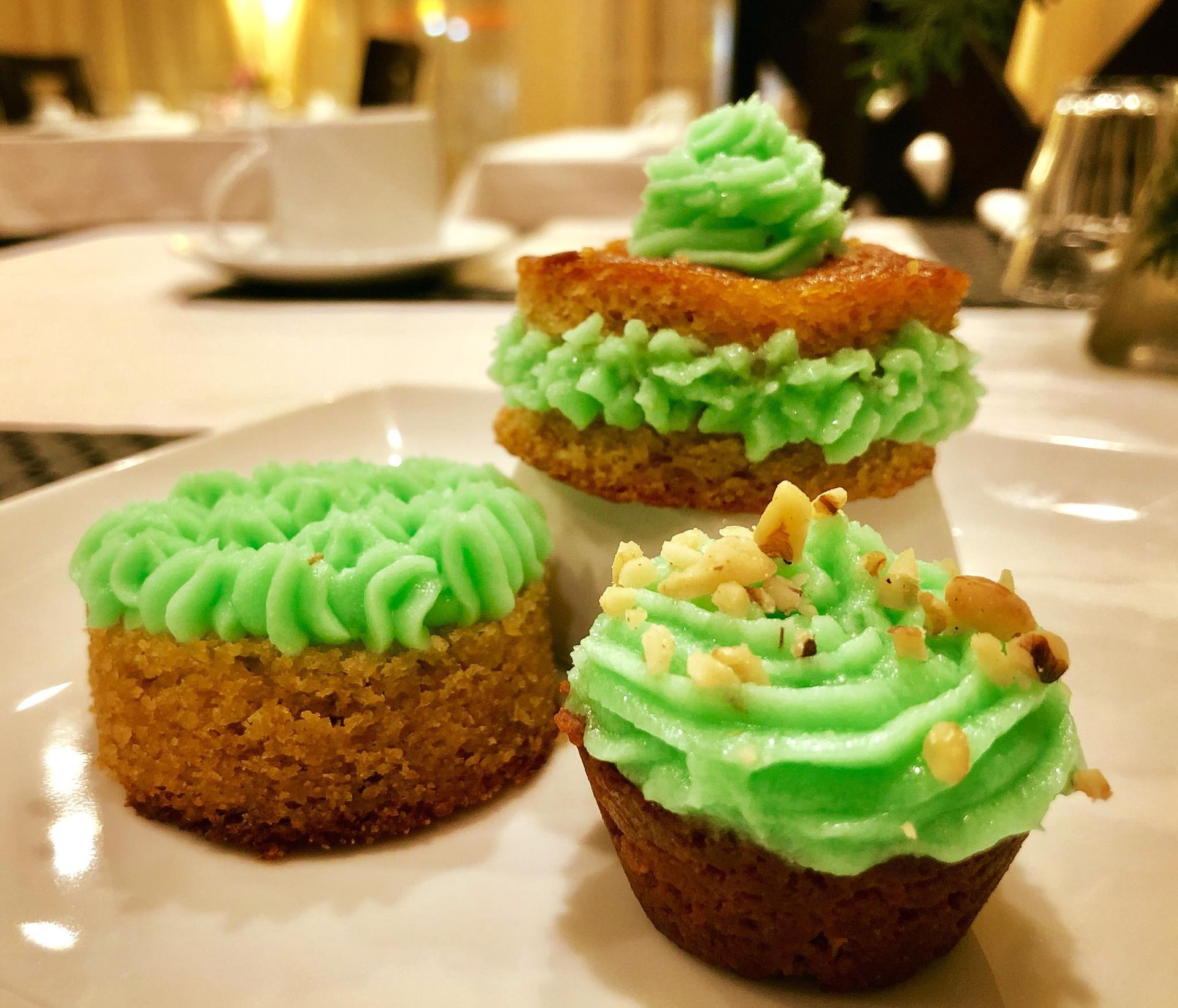 Three small, round cakes with green frosting on a white plate. One is stacked, two are topped with nuts.