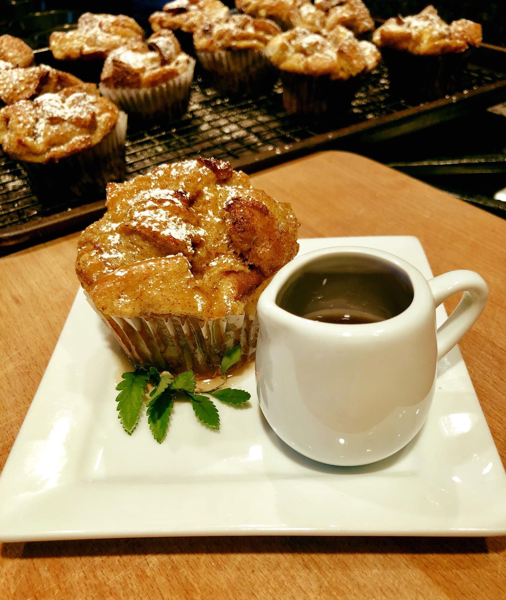 Muffin with syrup and mint sprig on a white plate, with more muffins in the background.