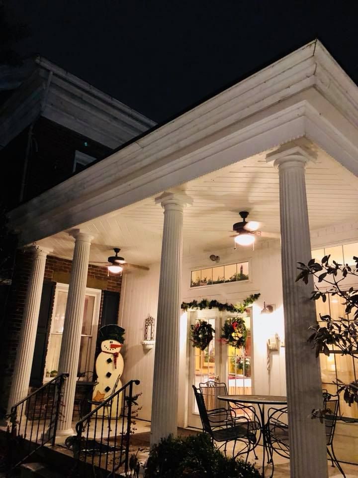Lit porch decorated for Christmas with snowman, wreaths, columns, and outdoor furniture.