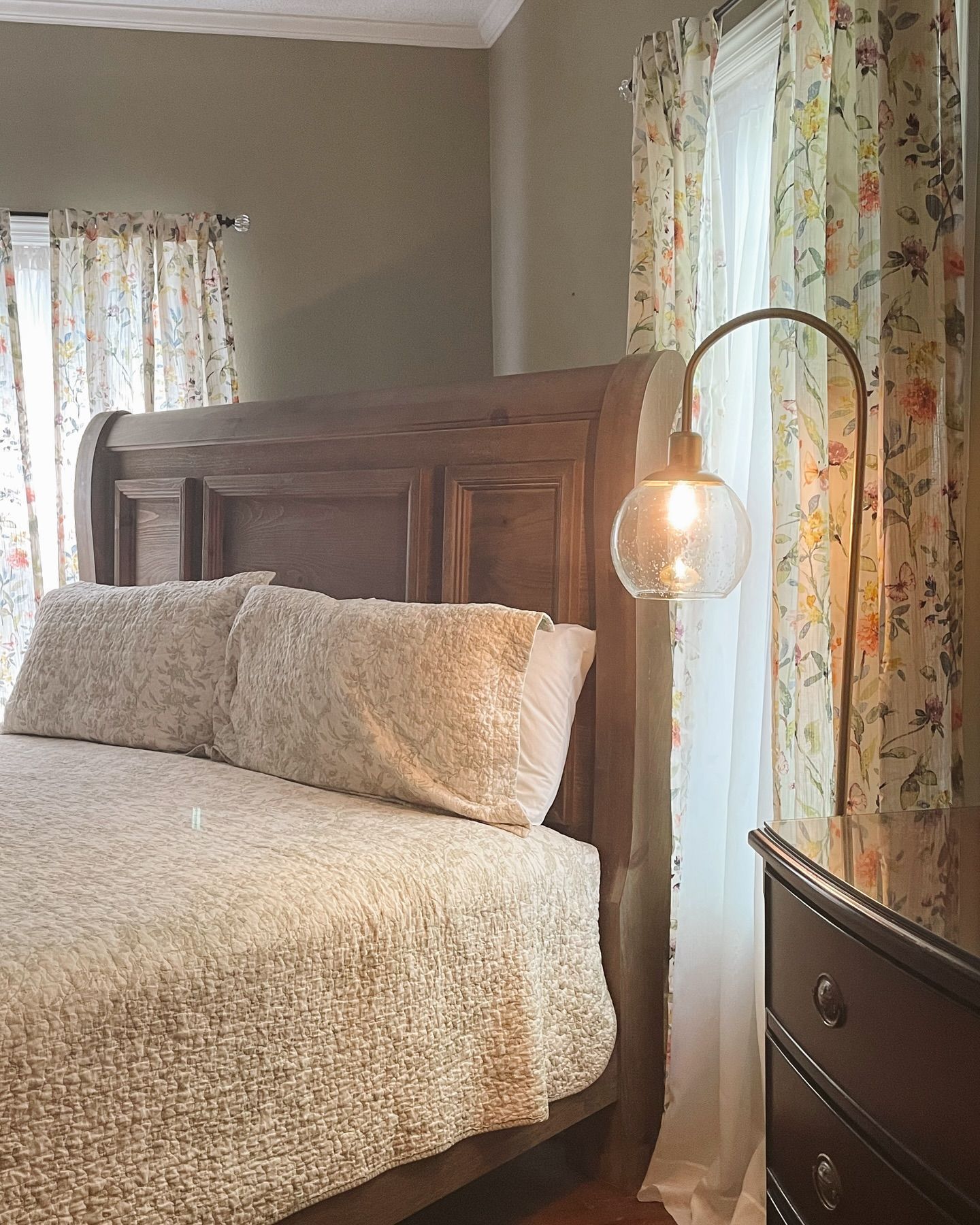 Bedroom with wooden bed, floral curtains, and a lamp with a globe bulb.