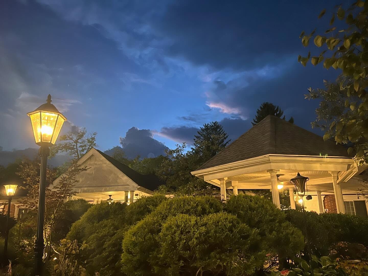 A gazebo and building with lit lanterns against a blue and dark cloudy sky.