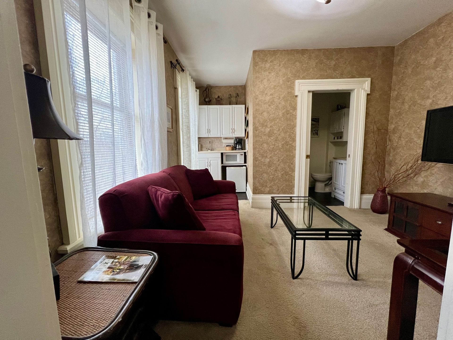 Cozy living room with a red couch, small kitchenette, and bathroom visible in the doorway.