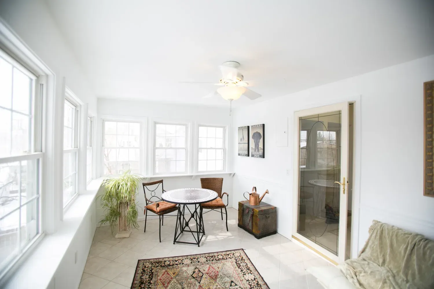 Sunroom with white walls, windows, table, chairs, rug, and a chest.