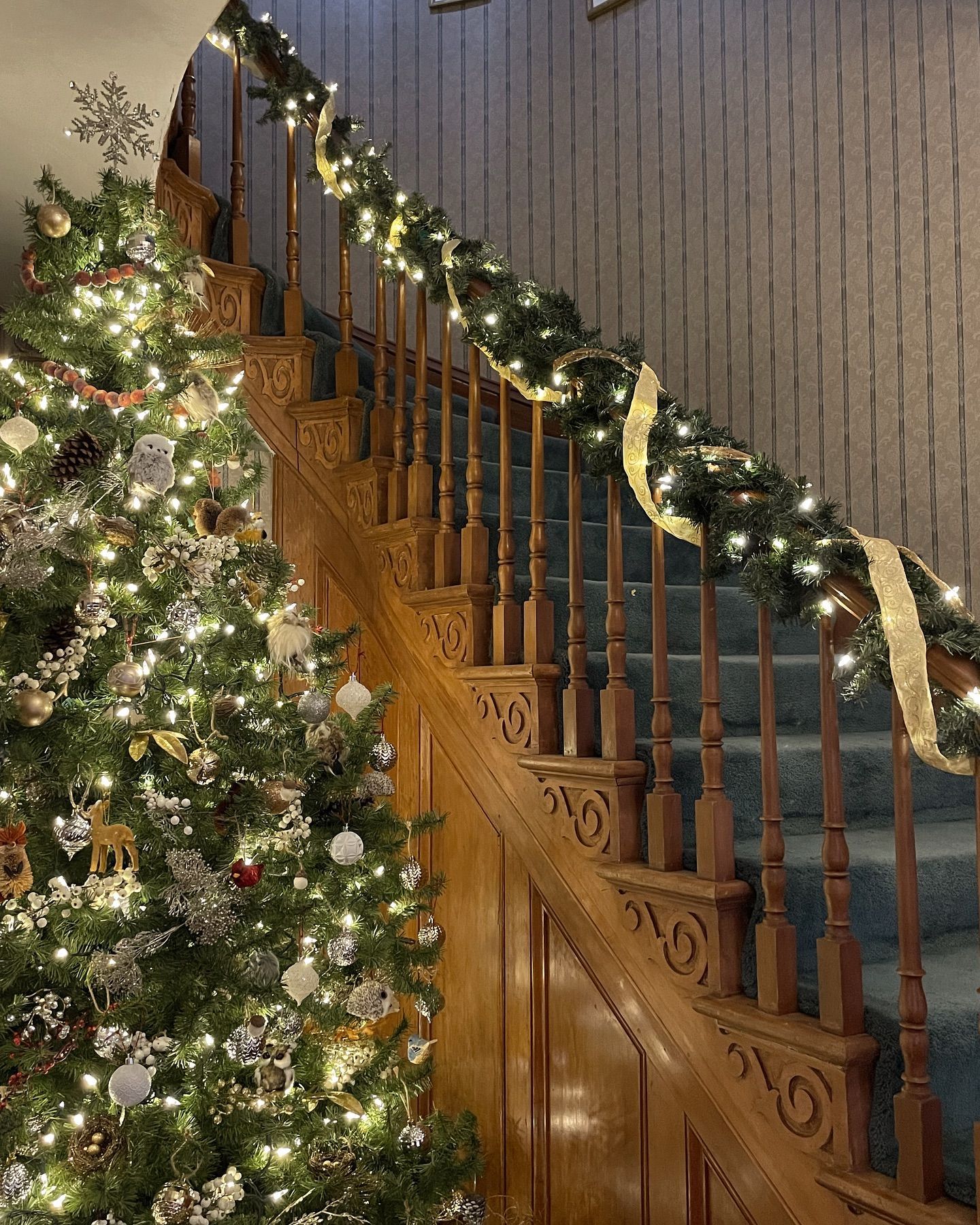 Christmas tree beside a wooden staircase decorated with garland and lights.