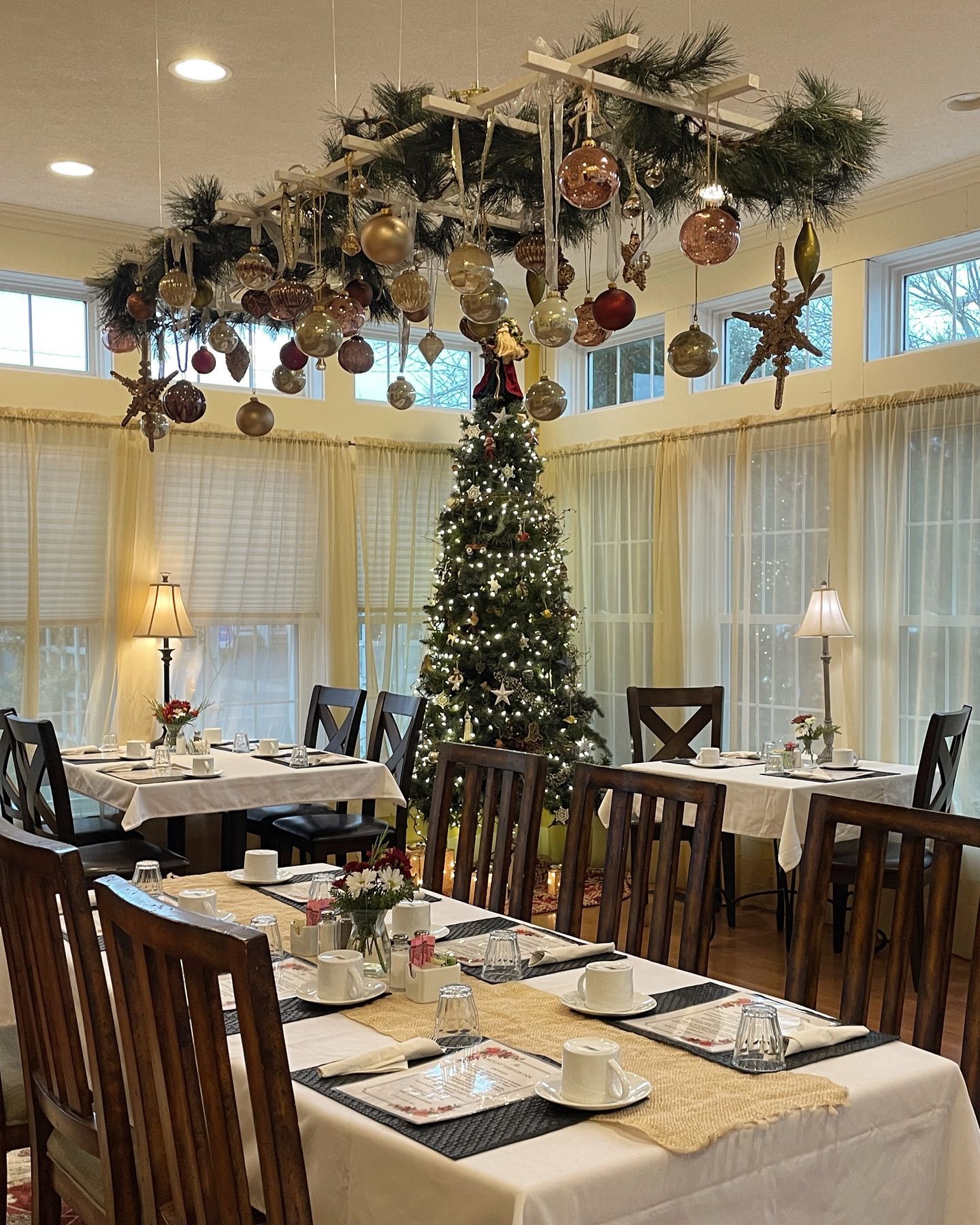 Dining room decorated for Christmas, with a decorated tree, tables set for a meal, and overhead decorations.