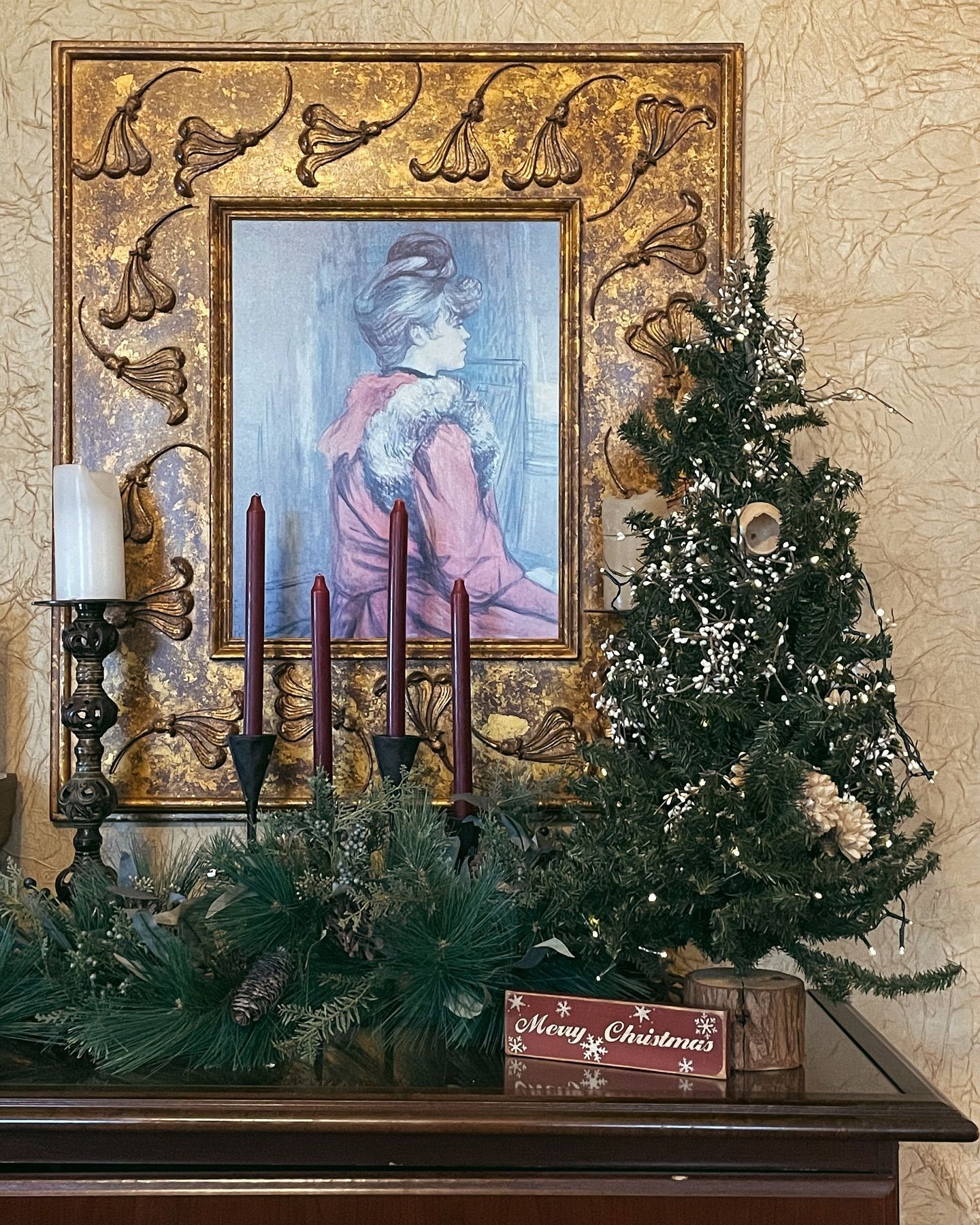 Christmas display with a painting, small tree, candles, and garland.